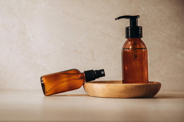 The concept of organic cosmetics. Bottles with face lotion on a beige background with a wooden plate - Fotografie, Obrázek
