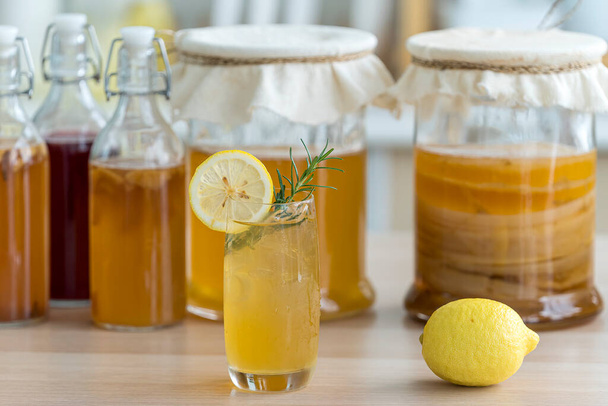 Kombucha tea with lemon and sweetened root filling in glass jug on kitchen background. Natural kombucha fermented tea beverage healthy organic drink in glass. - Фото, изображение