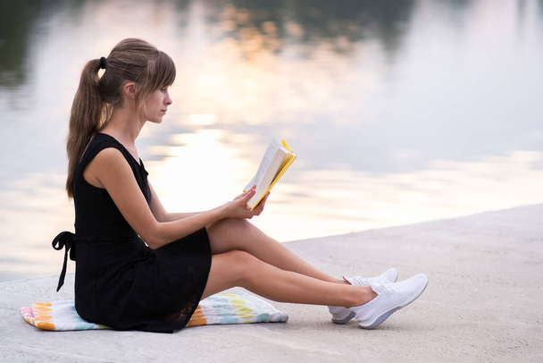 Naisopiskelija istuu kesäpuistossa lukemassa oppikirjaa ulkona. Koulutus ja sudy käsite - Valokuva, kuva