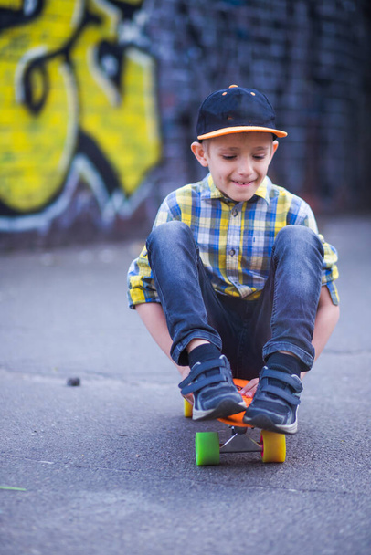 Poika ratsastaa skeittilaudalla. Lapsi kävelyllä ympäri kaupunkia taustalla graffiti seinillä. aktiivinen harrastus, urheilu ja terveys - Valokuva, kuva