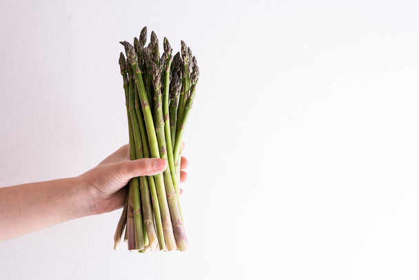 Female hand holding a bunch of raw asparagus on a white background, healthy vegan food. - Fotografie, Obrázek