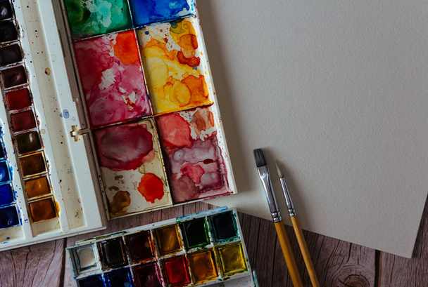 Palette of watercolor paints, blank paper and brushes on wooden background.  Artist's work space. Copy space. Selective focus. - Foto, imagen