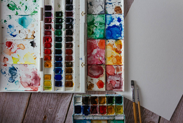 Palette of watercolor paints, blank paper and brushes on wooden background.  Artist's work space. Copy space. Selective focus. - Fotografie, Obrázek