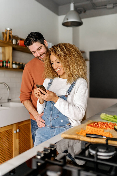 Couple looking at a smartphone in kitchen. - Φωτογραφία, εικόνα