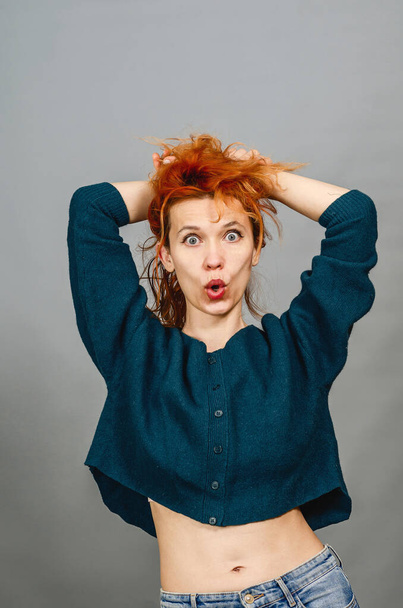 Surprised young woman with red hair. Hands holding hair. Green sweater. Naked thin waist. Surprise after losing weight - Foto, Imagem