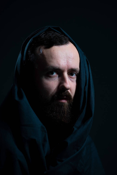 dramatic religious portrait of a bearded guy in a black cape on a dark background. - Foto, Imagem
