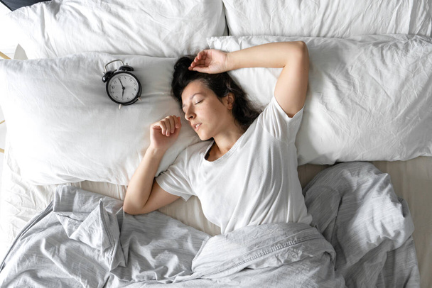 Top view of a girl sleeping next to an alarm clock. Time to wake up. On the wake-up clock 7 a.m. Deep sleep - Fotoğraf, Görsel