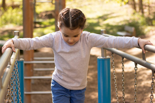 Schoolgirl in a gray turtleneck sweater and blue jeans plays on the playground - 写真・画像