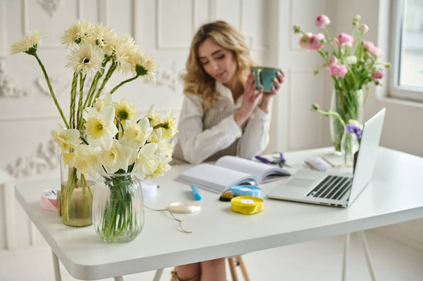 Young creative woman in a flower shop, using laptop. A startup of florist business. - Foto, imagen