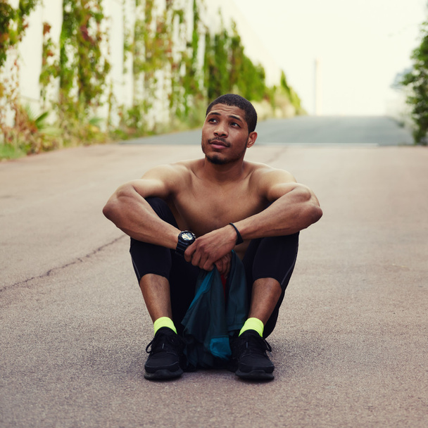 Athletic male runner resting after training outdoors while sitting on the ground - Fotó, kép