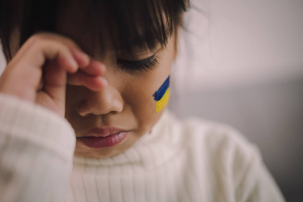 Un niño con la bandera de Ucrania está llorando. Tristeza anhelando esperanza. Las lágrimas de los niños de la guerra. Evacuación de civiles. Libertad para Ucrania - Foto, imagen