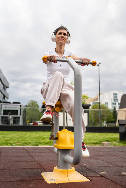Jedna kobieta nowoczesny dojrzały kaukaski kobieta z krótkim treningiem włosów przed budynkiem w dzień na rowerze trener symulator maszyny na zewnątrz siłownia Sport fitness zdrowy styl życia koncepcja kopiuj przestrzeń - Zdjęcie, obraz