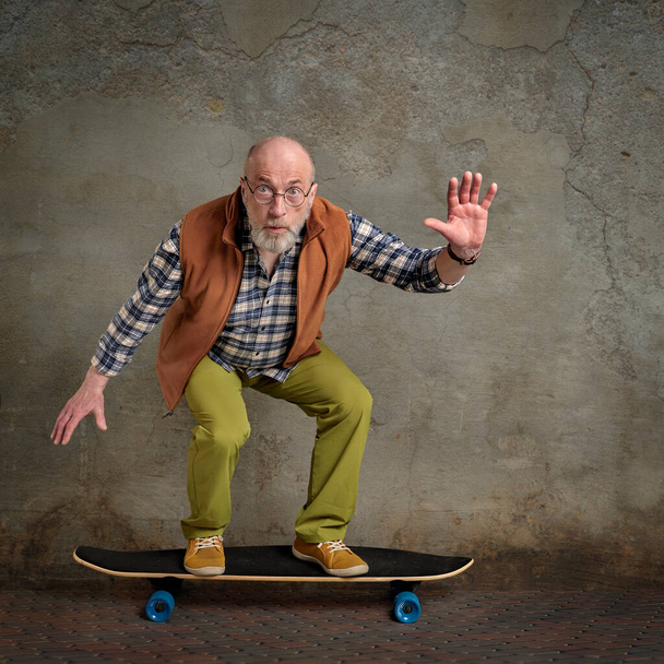 scared bearded senior man riding long skateboard in a grunge urban environment - 写真・画像