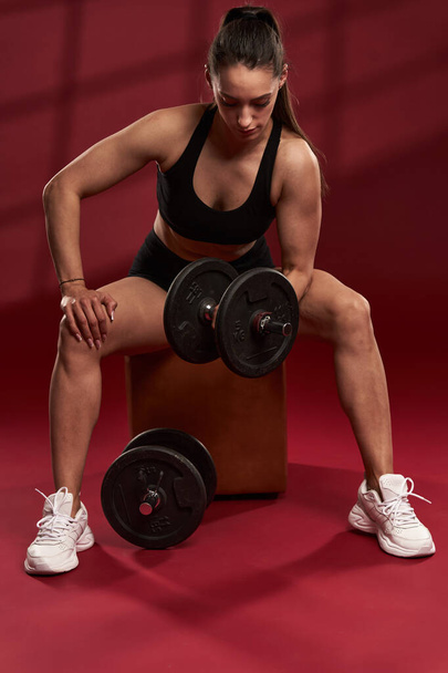 Strong woman doing biceps curl exercise with dumbbells, seated - Φωτογραφία, εικόνα