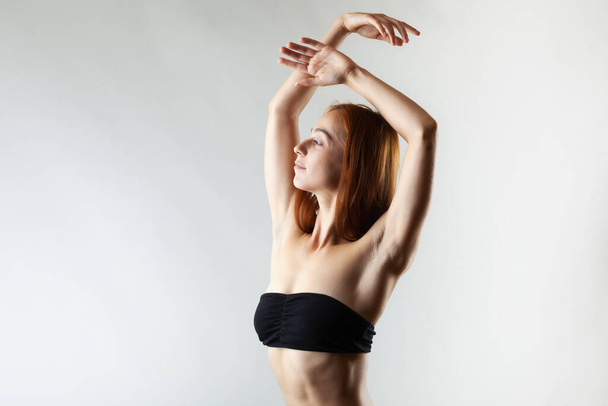Beautiful girl with burnt orange hair stretching and making ballet pose. Studio portrait on gray background. - 写真・画像