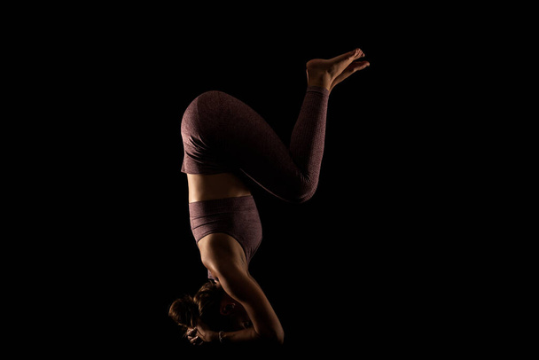 Fit woman practicing yoga poses. Side lit half silhouette girl doing exercise in studio against black background. - Foto, immagini