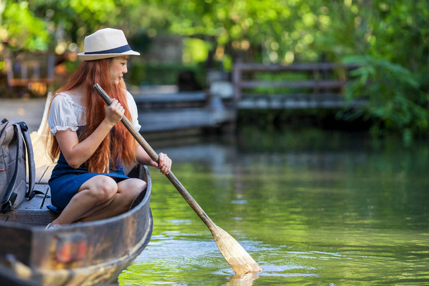 Young Asian woman traveller is rowing wooden boat using old paddle during her travel to Thailand and visiting the local floating market with serene tropical nature of Southeast Asia - Fotó, kép