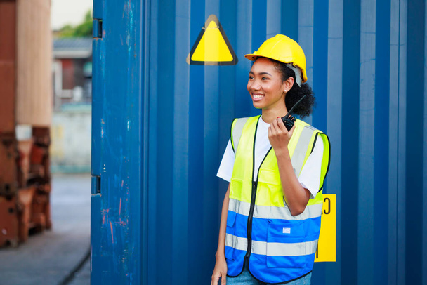 Black female dock worker control loading containers box from cargo at warehouse container yard. Marine and carrier insurance concept. cargo shipping container box in logistic shipping yard - Фото, изображение