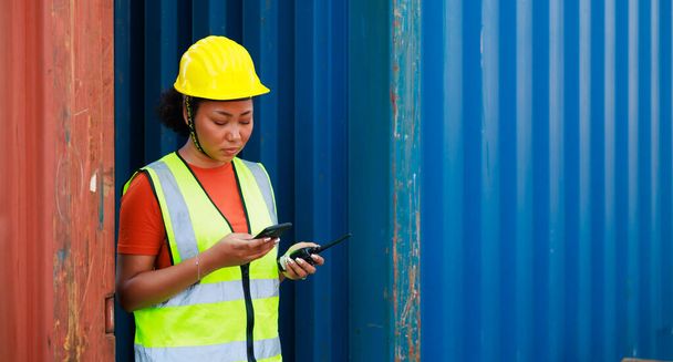 Online working by smartphone. Black female dock worker control loading containers box from cargo at warehouse container yard. Marine and carrier insurance concept. logistic shipping yard - Foto, immagini