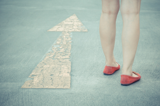 Винтажный тон девушки носить красные туфли пешком с желтой стрелкой движения указатель на асфальтовом фоне дороги - Фото, изображение