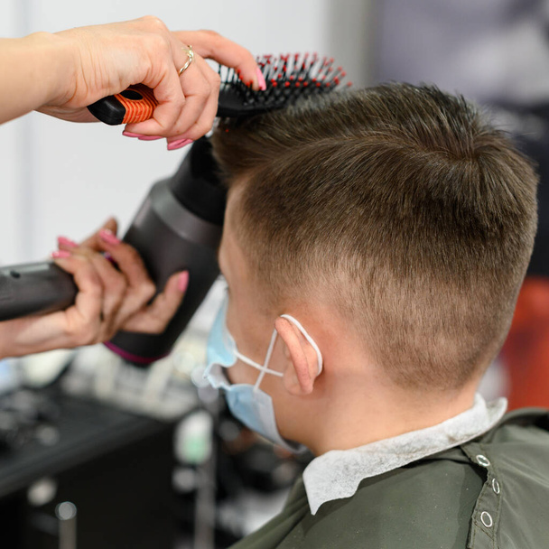 Подросток стрижется во время пандемии в парикмахерской, стрижется и сушит волосы после стрижки, укладка волос после стрижки с феном. - Фото, изображение
