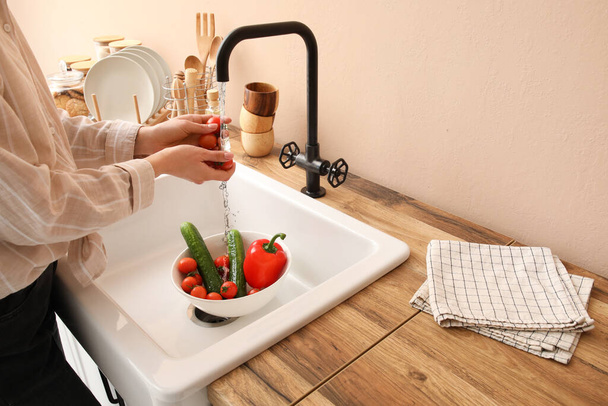 Woman washing fresh vegetables in kitchen sink  - Фото, изображение