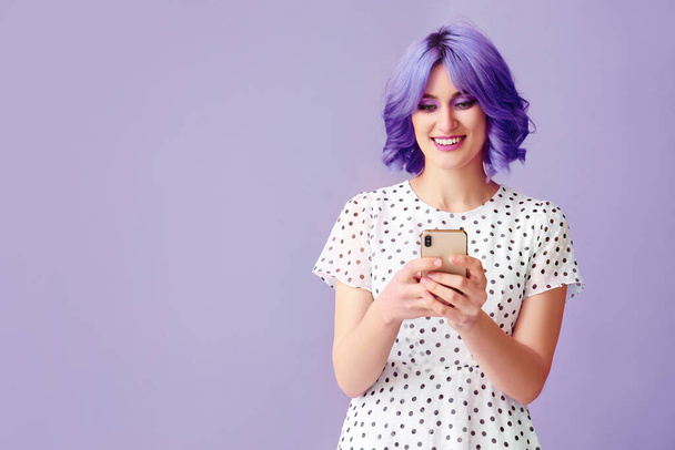Tyylikäs nuori nainen, jolla on kirkkaat hiukset ja matkapuhelin väritaustalla - Valokuva, kuva