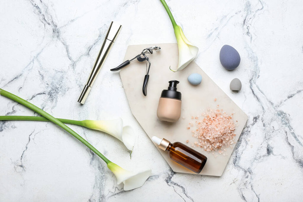 Composition with cosmetics, makeup sponges, eyelash curler and calla lilies on light background - Fotó, kép