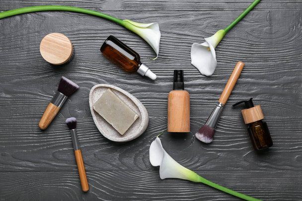 Composition with cosmetic products, makeup brushes and calla lilies on dark wooden background - Fotoğraf, Görsel