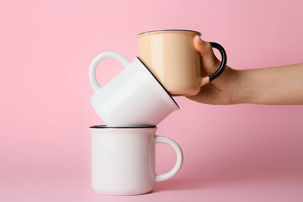 Female hand with ceramic cups on pink background - Fotó, kép
