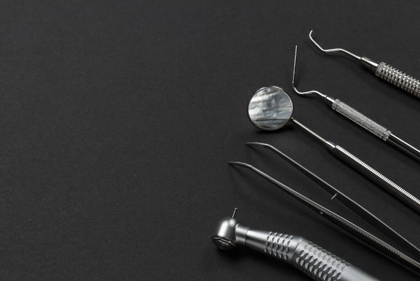 High-speed dental handpiece with bur, tweezers, a mouth mirror, a plugger and a curette on the black background. Medical tools. - Foto, imagen