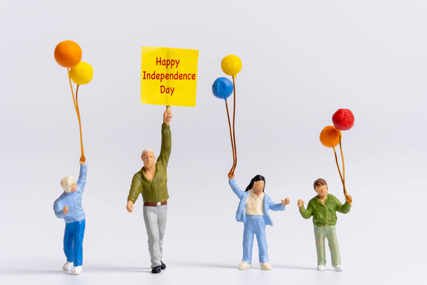 Miniatuur mensen met vlaggen met woord Gelukkige Onafhankelijkheidsdag op grijze achtergrond - Foto, afbeelding