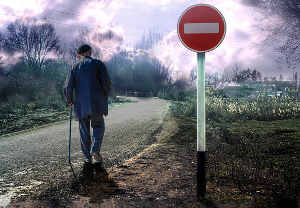 An elderly man with a crutch on the road under a forbidding road sign. - Fotoğraf, Görsel