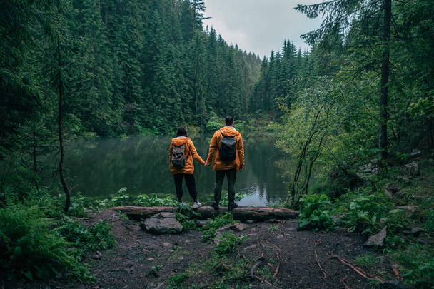 couple hikers in yellow raincoat looking at mountain lake backpackers - Photo, Image