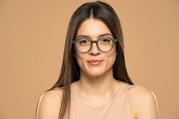 Porträt einer jungen schönen Frau mit Brille auf beigem Hintergrund. - Foto, Bild