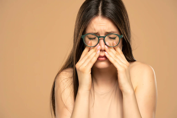 Sinusschmerzen, Sinusdruck, Sinusitis. Traurige Frau mit Brille und Nasennebenhöhlenschmerzen auf beigem Hintergrund. - Foto, Bild