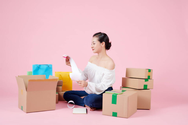 Joven mujer asiática startup pequeña empresa freelance sentado con caja de paquete, móvil y recibo de venta en el piso en la sala de estar en casa - Foto, imagen
