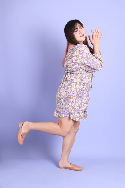 The chubby Asian woman standing on the purple background with the casual clothes. - Foto, afbeelding