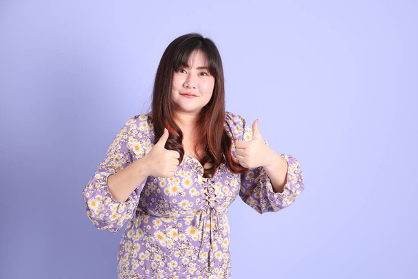 Толстая азиатка, стоящая на фиолетовом фоне в повседневной одежде. - Фото, изображение
