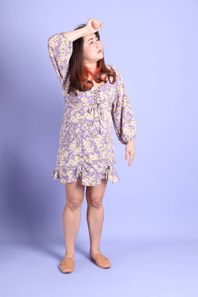 The chubby Asian woman standing on the purple background with the casual clothes. - Foto, imagen