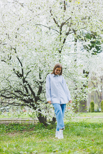 A woman in a white shirt and jeans with glasses in her hands in a spring garden. - Photo, Image