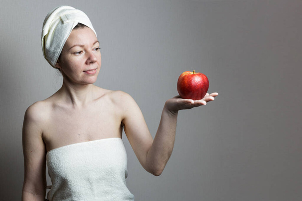 Μια νεαρή γυναίκα μετά από ένα μπάνιο με πετσέτα. μια γυναίκα κρατά ένα μήλο στην παλάμη της. - Φωτογραφία, εικόνα