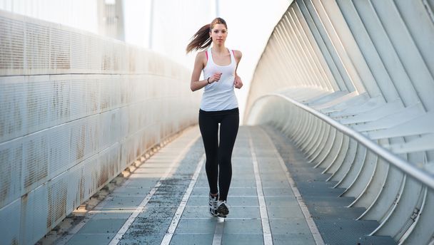 Young woman running outdoors on a modern bridge. - Zdjęcie, obraz