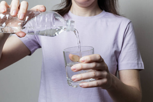 girl pours water into a glass. girl in a purple t-shirt. Healthy food concept - Photo, image