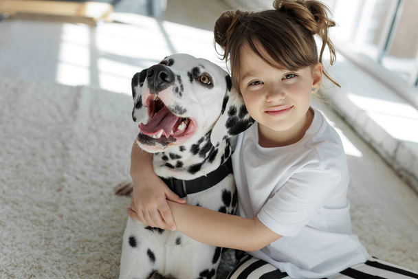 Dziecko z psem. Szczęśliwa dziewczyna leży na dywanie z dalmatyńskim psem. - Zdjęcie, obraz