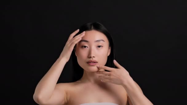 Idealna koncepcja skóry. Piękny portret młodej azjatyckiej damy pieszczącej jej twarz, cieszącej się kondycją skóry, patrzącej w kamerę - Materiał filmowy, wideo