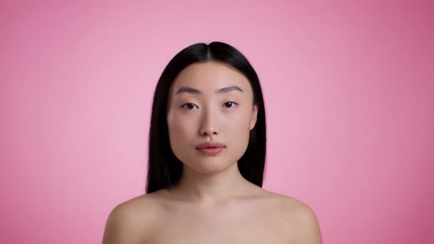 Természetes ázsiai szépség. Vonzó koreai nő csupasz vállak pózol és mosolyog a kamera, rózsaszín stúdió háttér - Felvétel, videó