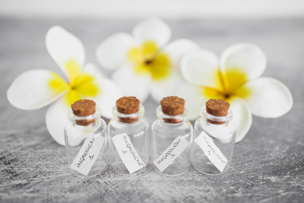 маленькі пляшки інгредієнтів з квітами на задньому плані, концепція природної краси та органічних інгредієнтів в скінарі
 - Фото, зображення