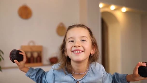 Petite fille émotionnelle heureuse tenant des cupcakes dans les mains couvrant les yeux à la maison, souriant enfants heureux aimant concept doux et sucre nutrition - Séquence, vidéo