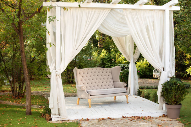 Açık hava terası. Dışarıda dinlenmek için çardak. Bahçede, Provence tarzı veya kırsal tarzında kanepe olan bir podyum var. Düğün süslemeleri. Beyaz perdeleri akan yaz çardağı. Romantik oyuk - Fotoğraf, Görsel